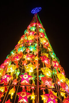 Colorful illuminated Christmas tree made of glowing star lanterns at night festive holiday decoration