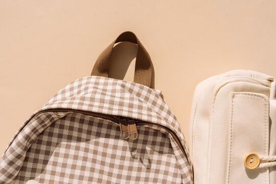Checkered backpack and beige pencil case in warm sunlight, stylish back to school concept.