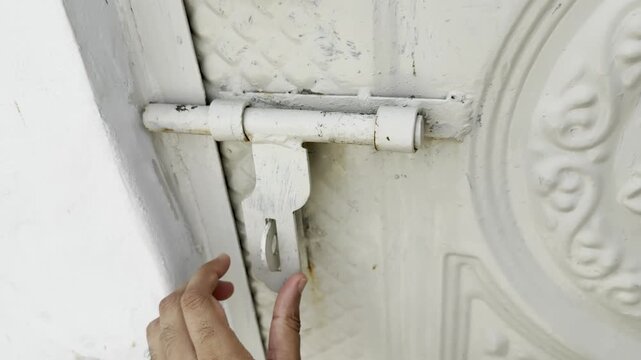 Hand sliding a white metal bolt on a textured vintage door to lock the mechanism in this close up video