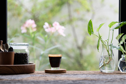 Coffee glass cup and roasted coffee beans on wooden table with flowers background