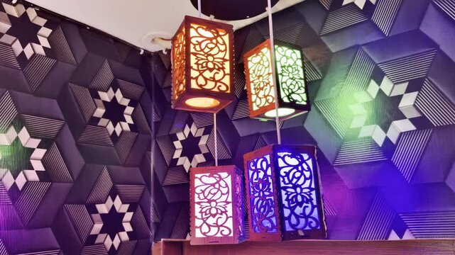 Glowing decorative lantern lamps suspended from ceiling create colorful motion effect against textured geometric patterned wall in this video footage
