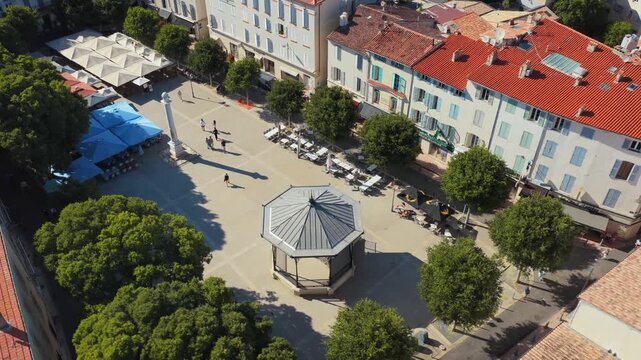 Aerial view of sunny village town square with bandstand and restaurant seating in southern france.