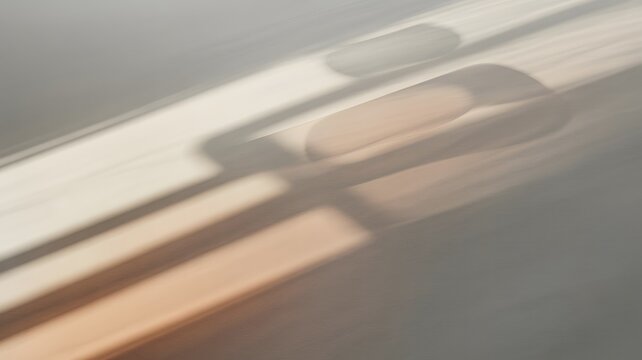 Abstract light shadows cast across a smooth grey surface creating soft geometric shapes with warm golden beige and subtle tones