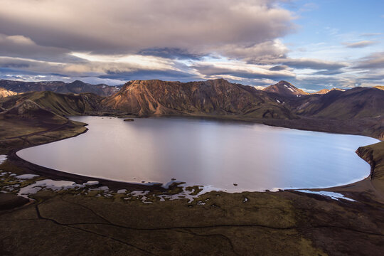 Aerial view of a serene lake surrounded by volcanic mountains and rugged terrain in Iceland.