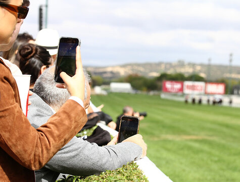Fotografiando p&uacute;blico haciendo fotos en hip&oacute;dromo y espectadores grabando v&iacute;deo de carrera de caballos 