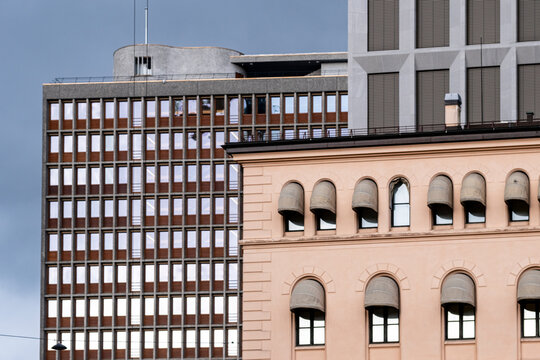 Arched windows anchor the frame as an older facade rises before modern buildings in Oslo, Norway, where historic architecture meets overcast light in clear contrast.