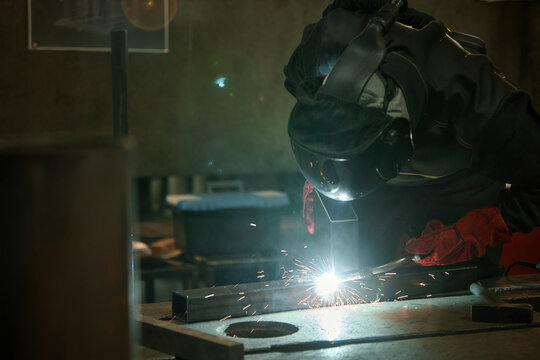 Male welder in protective mask welding metal in workshop, creating bright sparks. Image suitable for industrial manufacturing and vocational training promotions