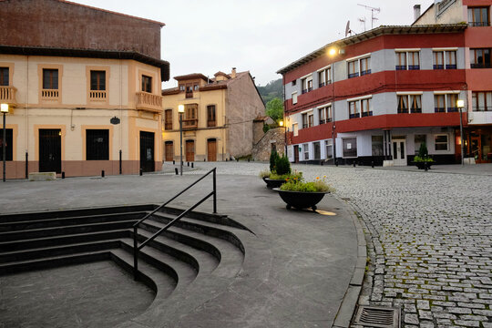 Empty cobblestone square with modern semi-circular stairs, large planters, and illuminated street lamps at dusk in the historic town of Salas, Asturias, Northern Spain.