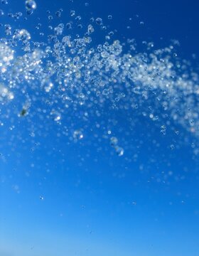 鮮やかな青空を背景に太陽の光を浴びてキラキラと輝く噴水の水滴と水しぶき　Sparkling Water Droplets and Splashes with Bright Sunlight against a Vibrant Blue Sky
