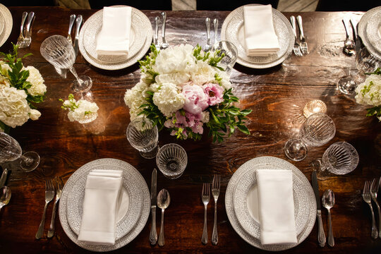 A well-arranged table set for a meal. Plates, cutlery, and glasses are neatly placed around a floral centerpiece with various flowers