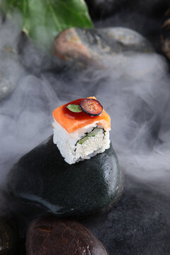 Salmon and cheese rolls on black stone in clouds of white smoke. Restaurant dish. Food photography in style of molecular cuisine or premium restaurant