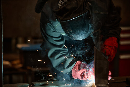 Male welder in protective mask welding metal parts in workshop. Image represents industrial manufacturing and is suitable for trade school marketing, close up shot