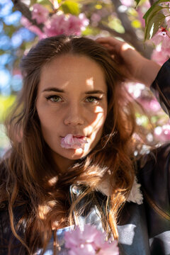 Woman Cherryblossom Spring: Girl with blossom in mouth poses outdoors under blooming pink flowers tree.