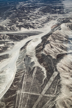 Aerial view of the Nazca Lines geoglyphs etched into the arid desert landscape with rugged mountains and dry riverbeds in Nazca Province, Ica, Peru.