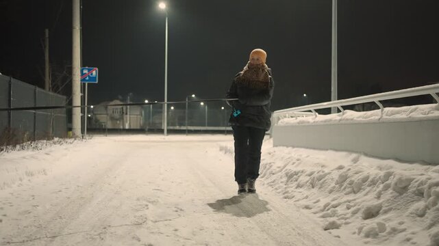Woman walking her dog on a snowy street of a suburban area at night