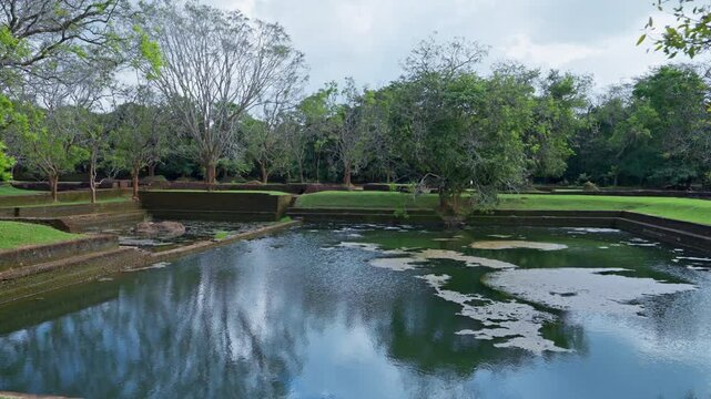 Still water of an ancient bathing pool reflects clouds and trees within the royal water gardens of the Sigiriya fortress complex in Sri Lanka.