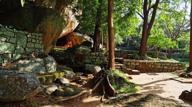 Ancient stone walls and a rock shelter stand among huge boulders and trees in the boulder gardens at the foot of Sigiriya rock in Sri Lanka.