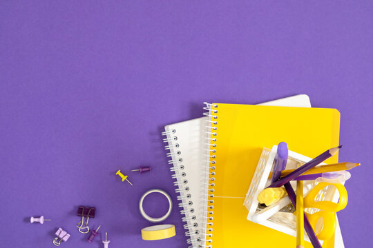 Purple and Yellow School Office Stationery Bottom Border Background with Copy Space. Spiral Notebooks, Pencils, Tape and Clips on Violet Desk Top View. Creative Workspace Back to School Concept.
