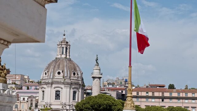 National tricolour flag flutters beside a historic church dome and Trajan Column over the central city skyline.