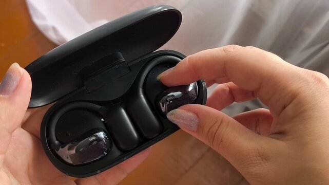 Woman taking wireless earbud from charging case, true wireless earphones, music listening and mobile audio concept.