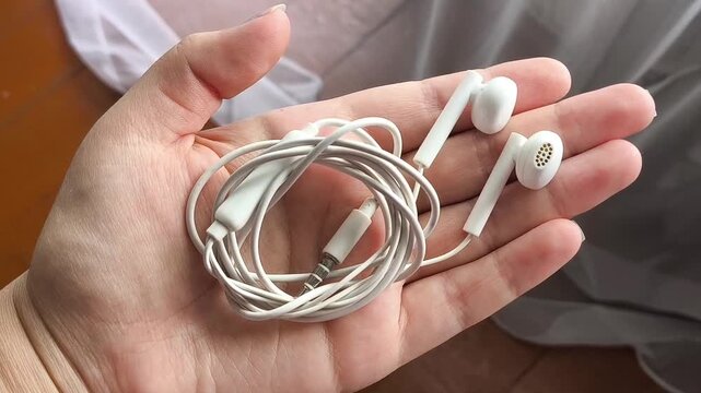 Wired earphones held in woman's hand, portable audio device, music listening and everyday technology concept.