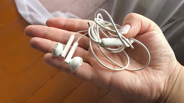 Wired earphones held in woman's hand, portable audio device, music listening and everyday technology concept.