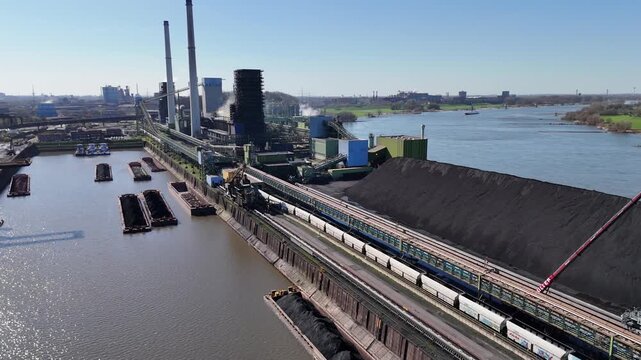 Drone advances toward a large coal stockpile and industrial plant built out on a river peninsula