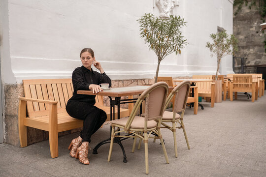 Pensive young woman sitting on wooden bench at outdoor cafe during quiet daytime break