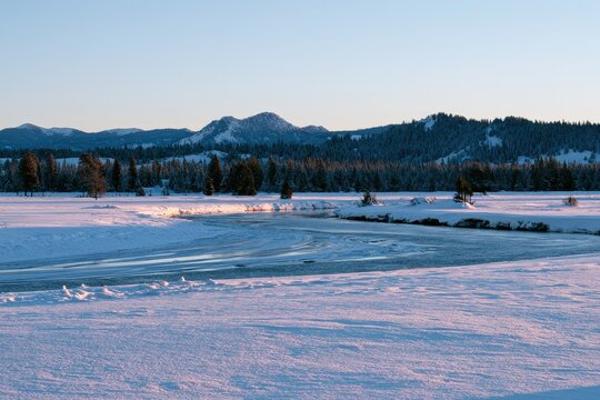 Snowy river valley in Island Park, Idaho: Henrys Fork region with pine forest and distant alpine peaks in winter