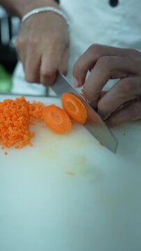 Close up vertical video of a professional chef using a sharp knife to slice a fresh carrot into clean round slices next to finely chopped carrots.