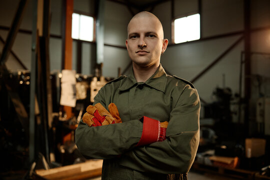 Portrait of young adult Caucasian male welder standing with arms crossed in industrial workshop. Image represents blue collar workforce and is suitable for trade school marketing