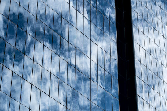 Passing clouds drift through a blue reflection across broad planes of glass, as the facade uses vertical windows to turn sky and building into contemporary architecture.