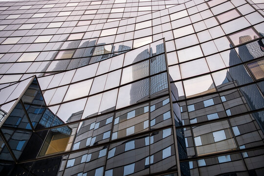 An upward view lets a glass facade fold each reflection through a precise grid, while windows break the nearby building into angles of urban architecture.