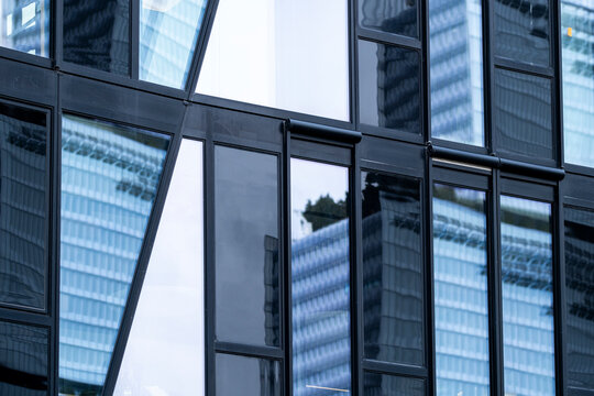 Dark framing divides the glass facade into windows that quietly hold each reflection, turning a nearby tower and urban building into abstract architecture.
