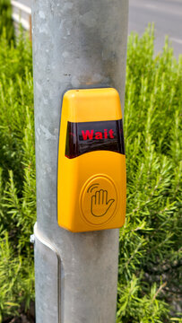 Yellow pedestrian crossing button displaying wait message on a street pole, featuring a touchless sensor for contactless activation and urban safety