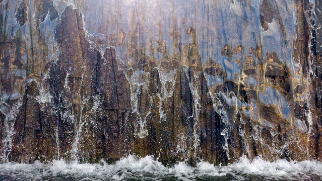 Water flowing down a textured stone wall, creating a dynamic waterfall and splashing into a pool below, depicting natural movement, power, and refreshing energy