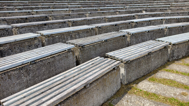 Rows of weathered concrete bleachers with wooden slats forming empty seating in an outdoor amphitheater. Creating a strong sense of repetition. Quietness