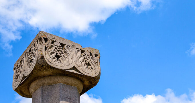 Ancient stone column capital from zvartnots cathedral ruins featuring intricate grape and acanthus leaf carvings under a bright blue sky with scattered clouds