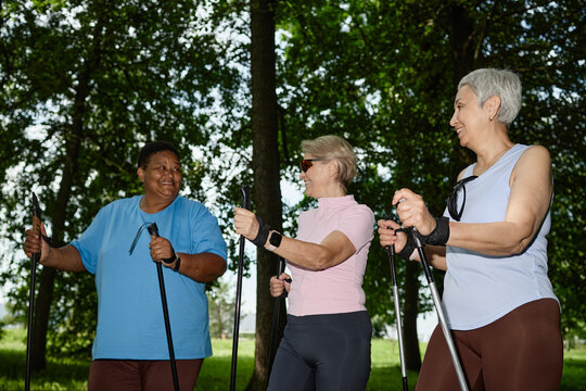 Diverse senior women practicing Nordic walking in park, smiling and talking. Image represents active aging and healthy lifestyle, suitable for retirement wellness campaigns, low angle view