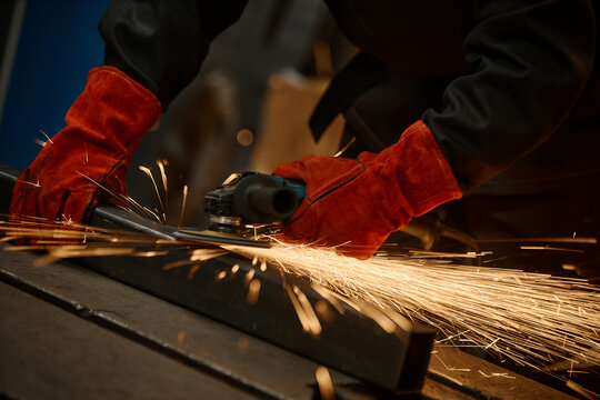 Hands of worker wearing protective gloves using angle grinder on metal with sparks flying. Image represents industrial manufacturing, suitable for trade school marketing, close up shot