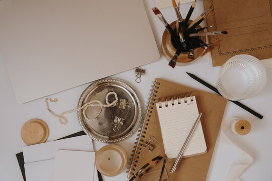 Aesthetic Flat Lay Desk Setup With Kraft Paper Notebooks, Laptop Edge, Silver Pen, And Paintbrushes