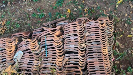 Neat stack of old terracotta clay roof tiles resting on the dry ground outdoors. © Rachmanul