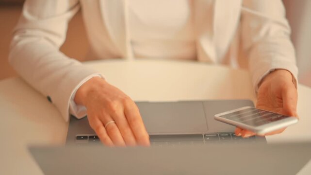 Business woman using a laptop and checking financial market data on a mobile phone.