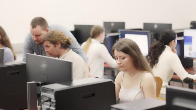 In group of students attending computer courses, female student attentively looks at monitor screen and does performs educational control work