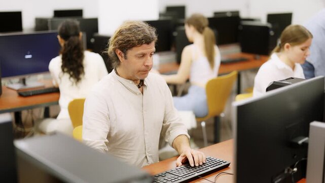 Side view on concentrated male student sitting at library desk with pc, preparing for exam in computer class. High quality 4k footage