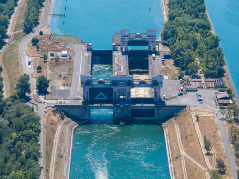 Aerial view of the Kembs lock on the Grand Canal d Alsace with concrete infrastructure and blue water surrounded by lush trees in Kembs, Grand Est, France.