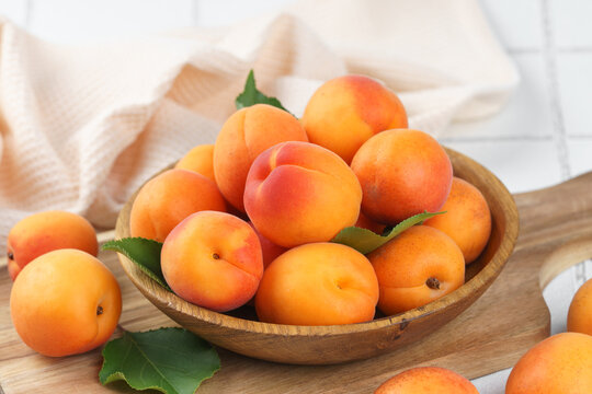 Close up of fresh ripe apricots in rustic wooden bowl with green leaves on yellow textured background. Healthy seasonal summer fruit, healthy food, nutrition, ingredient for cooking and desserts