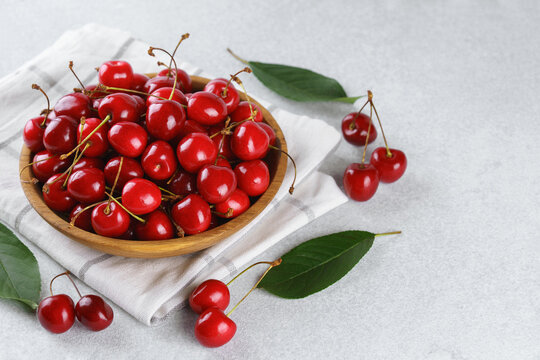 Fresh ripe sweet cherries in rustic wooden bowl with green leaves on light textured background. Top view flat lay with copy space. Juicy organic summer fruit, red berries, healthy seasonal food