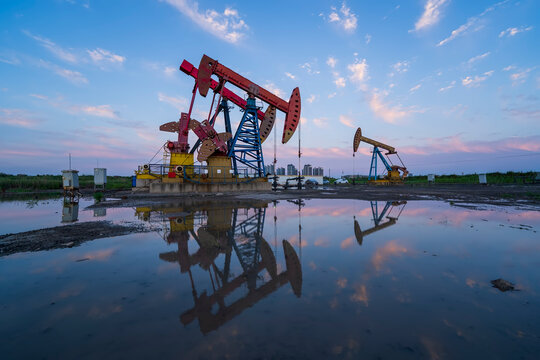 in the evening, oil pumps are running, The oil pump and the beautiful sunset reflected in the water, the silhouette of the beam pumping unit in the evening.