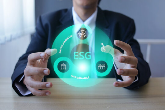 Businessman Gesturing With Both Hands Around Circular ESG Concept Graphic over Wooden Desk